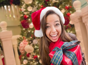 Girl wearing A christmas santa hat with bow wrapped gift in front of decorated tree