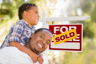 Happy african american father and mixed-race son in front of sold real estate sign
