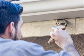 Professional painter using A brush to paint house fascia under rain gutter