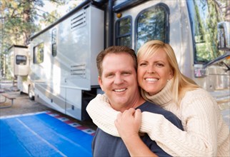 Happy caucasian couple in front of their beautiful RV at the campground