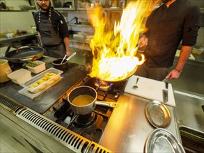 Chef cooking flambleing atlantic squid with olive oil in a big pan in a professional kitchen
