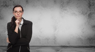 Young adult woman with pencil and glasses standing in front of blank grungy blank wall with copy space