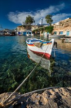 Fishing boats moored in crystal clear turquoise sea water in harbour in Greek fishing village of Mandrakia