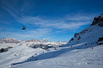 View of a ski resort piste with people skiing in Dolomites in Italy with cable car ski lift. Ski area Arabba. Arabba