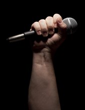 Color vertical microphone clinched firmly in male fist on a black background