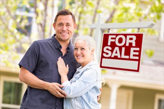 Caucasian couple in front of for sale real estate sign and house