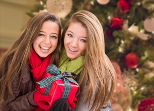 mixed-race young adult females holding A christmas gift in front of decorated tree