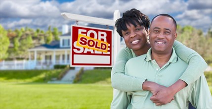 Happy african american couple in front of beautiful house and sold for sale real estate sign