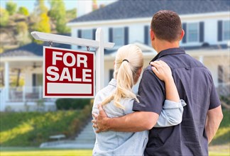 Young adult couple facing front of for sale real estate sign and house