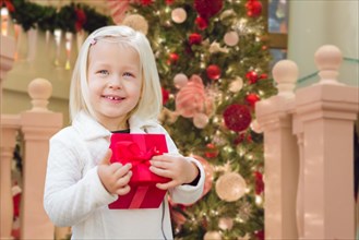 Happy young girl holding gift box in front of decorated christmas tree