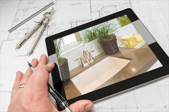Hand of architect on computer tablet showing luxury bathroom details over house plans