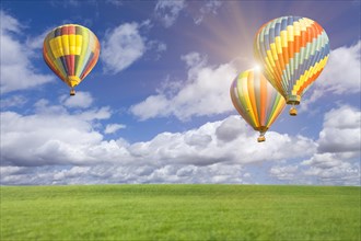Two hot air balloons up in the beautiful blue sky with grass field below