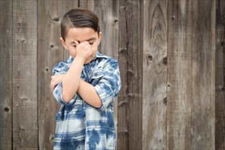 Young frustrated mixed-race boy with hand on face against wooden fence