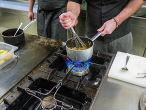 Chef using a hand mixer making a potato sauce cream reduction in a professional kitchen of a restaurant