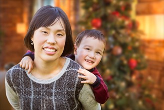 Chinese mother and mixed-race child inside house in front of decorated christmas tree