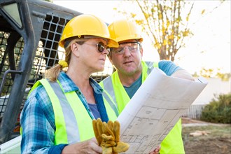 Male and female workers with technical blueprints talking at construction site