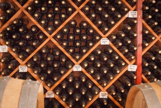 Several varietal wine bottles and barrels age inside dark cellar