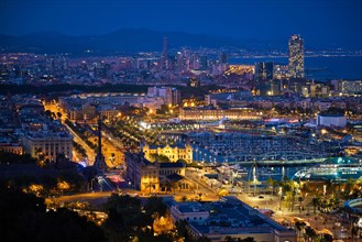 Aerial view of Barcelona city skyline with city traffic and port with yachts illuminated in the night. Barcelona