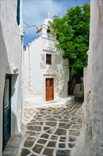Picturesque scenic narrow Greek streets with traditional whitewashed houses with blue doors windows of Mykonos town and orthodox church in famous tourist attraction Mykonos island