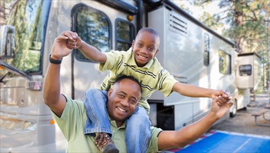 Happy african american father and son in front of their beautiful RV at the campground