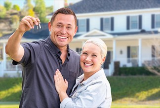 Young adult couple with house keys in front of beautiful home