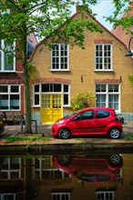 Red car on canal embankment in street of Delft with reflection