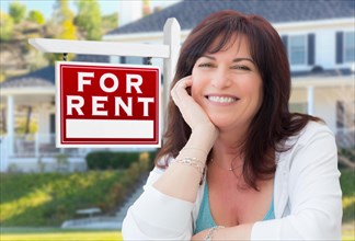 Middle aged woman in front of house with for rent real estate sign in yard
