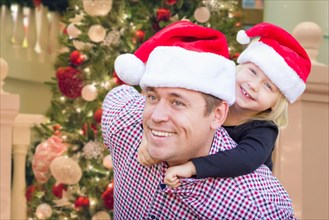 Father and daughter wearing santa hats in front of decorated christmas tree