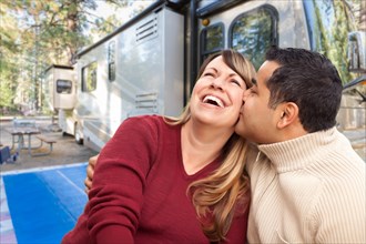 Happy mixed-race couple in front of their beautiful RV at the campground