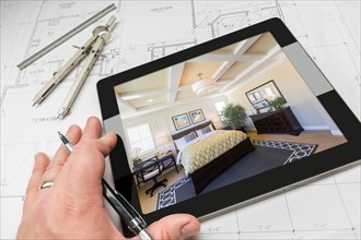Hand of architect on computer tablet showing custom master bedroom over house plans