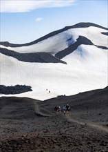 Hikers in barren hilly volcanic landscape of snow and lava fields