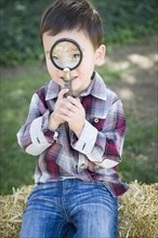 Cute young mixed-race boy looking through magnifying glass outside on hay bale
