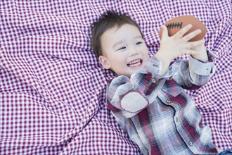Cute young mixed-race boy playing with football outside on picnic blanket