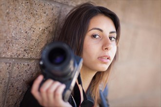 Young adult ethnic female photographer against wall holding camera