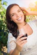 Beautiful young adult woman enjoying glass of wine tasting in the vineyard