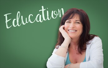 Education written on green chalkboard behind smiling middle aged woman