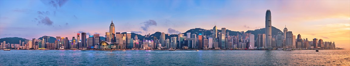 Panorama of Hong Kong skyline cityscape downtown skyscrapers over Victoria Harbour in the evening with junk tourist ferry boat on sunset with dramatic sky. Hong Kong