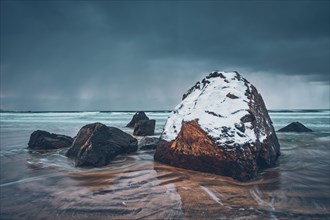 Rocks covered with snow on Norwegian sea beach in fjord in stormy weather with clouds. Skagsanden beach