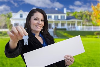 Hispanic woman holding blank sign and keys in front of beautiful house