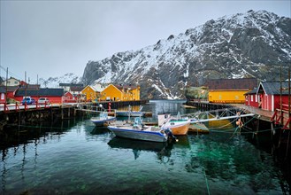 Pier with boats in Nusfjord authentic fishing village in winter with red rorbu houses. Lofoten islands