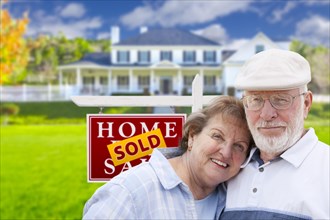 Happy affectionate senior couple hugging in front of sold real estate sign and house