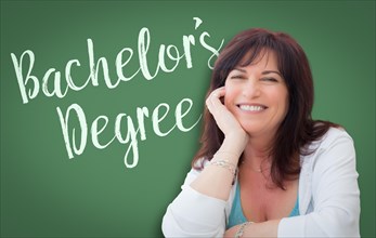 Bachelor's degree written on green chalkboard behind smiling middle aged woman