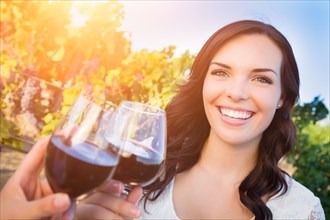 Beautiful young adult woman enjoying glass of wine tasting toast in the vineyard with friends