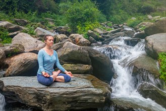Woman in Hatha yoga asana Padmasana outdoors at tropical waterfall