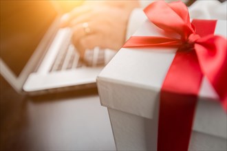 White gift box with red ribbon and bow near man typing on laptop computer