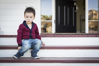 Cute melancholy mixed-race boy sitting on front porch steps
