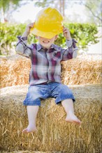 Cute young mixed-race boy laughing with hard hat outside sitting on hay bale