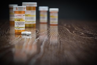 Variety of non-proprietary prescription medicine bottles and pills on reflective wooden surface
