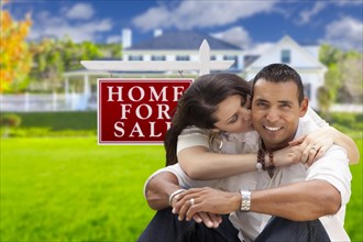 Young happy hispanic young couple in front of their new home and for sale real estate sign