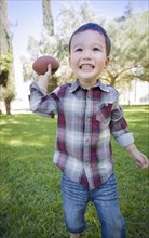 Cute young mixed-race boy playing football outside at the park